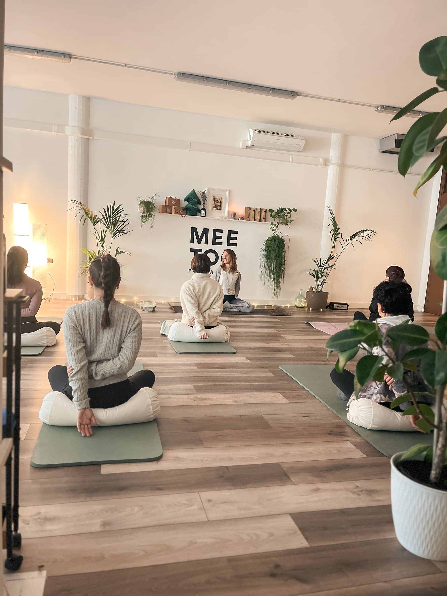 Lezione di yoga in gruppo nella sala di Mee Too Pilates, sedute sui cuscini davanti all'insegna
