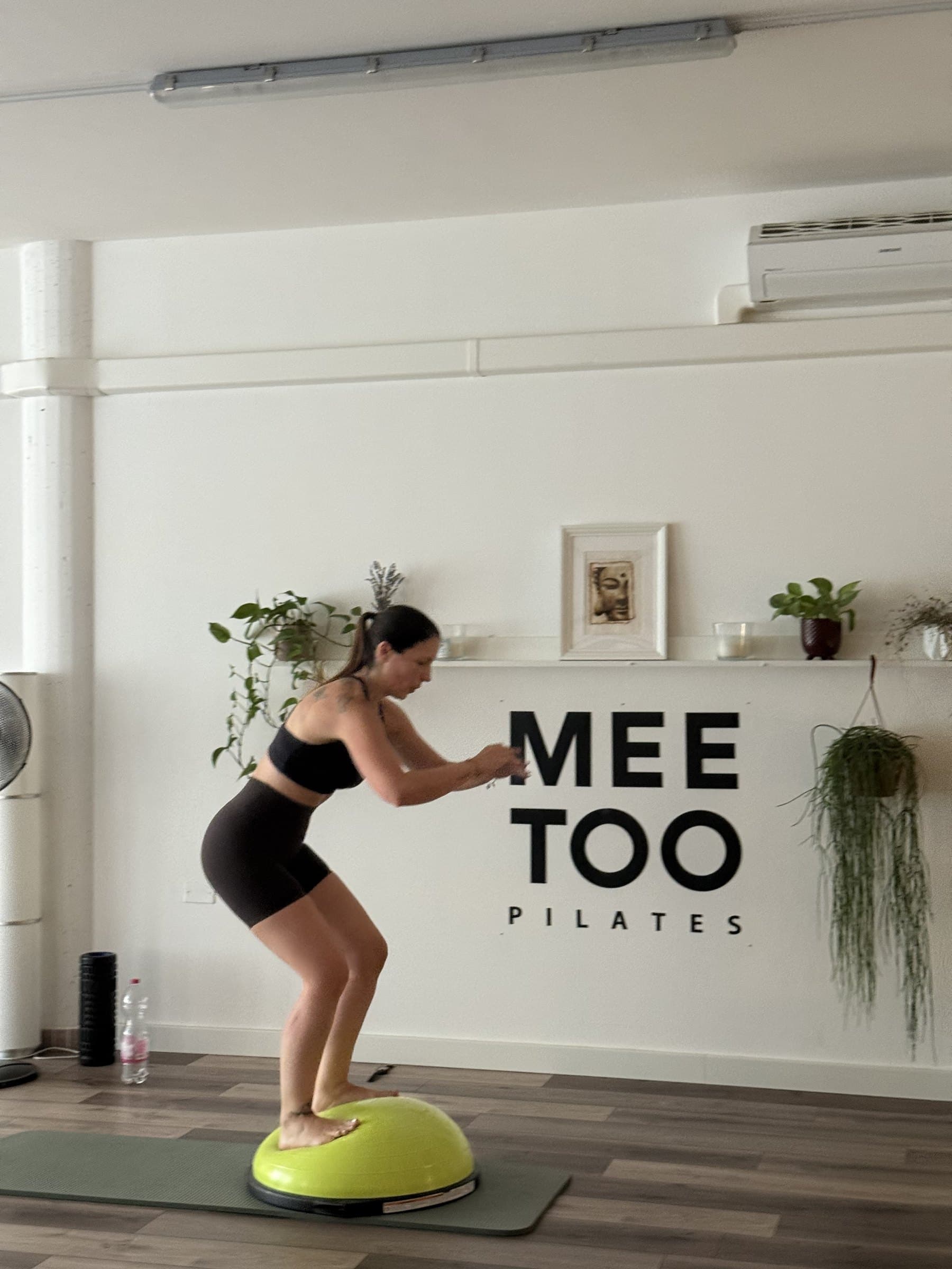 Squat in equilibrio sulla mezza sfera davanti all'insegna Mee Too Pilates
