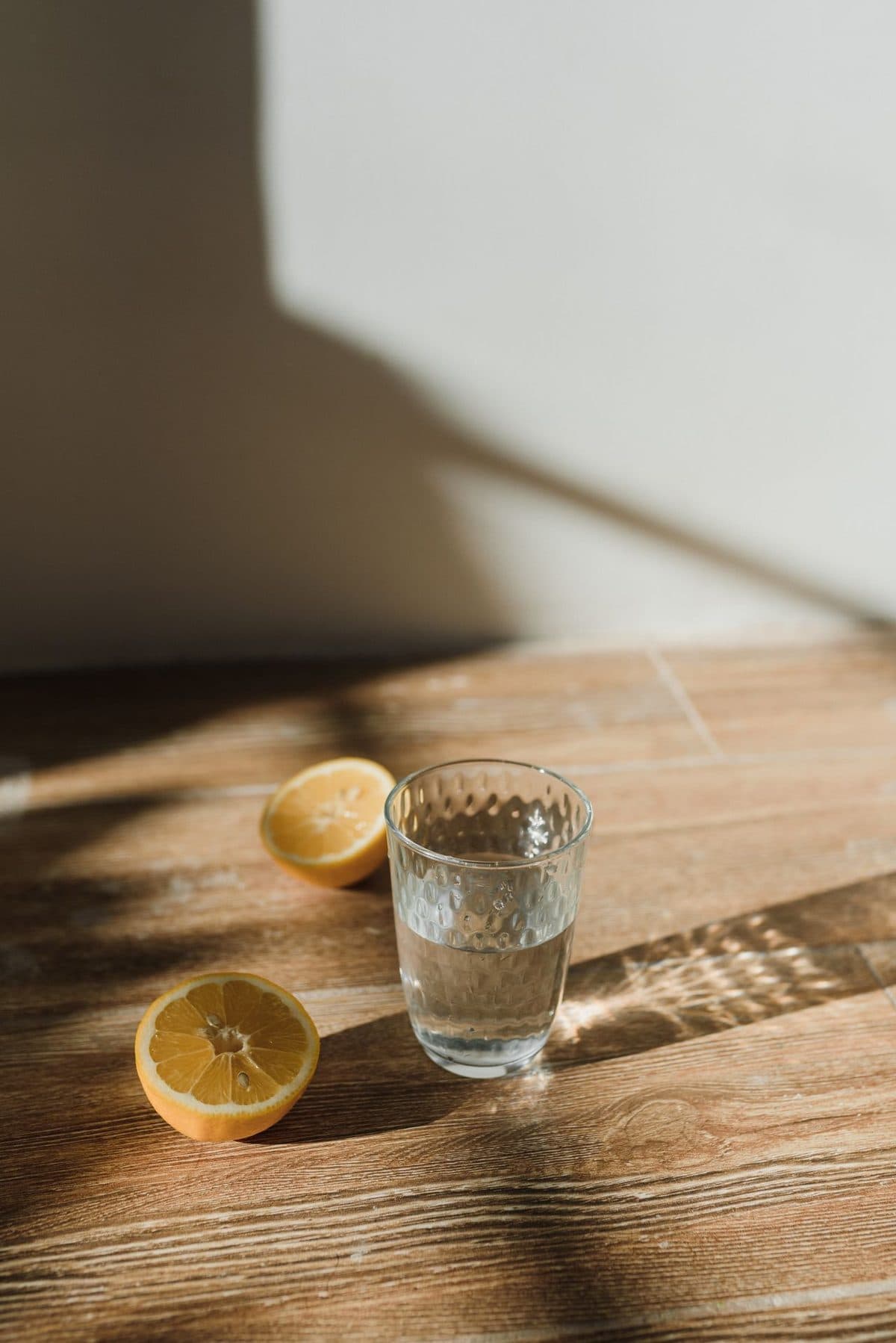 Due mezzi limoni e un bicchiere d'acqua su un tavolo di legno, nella luce del sole